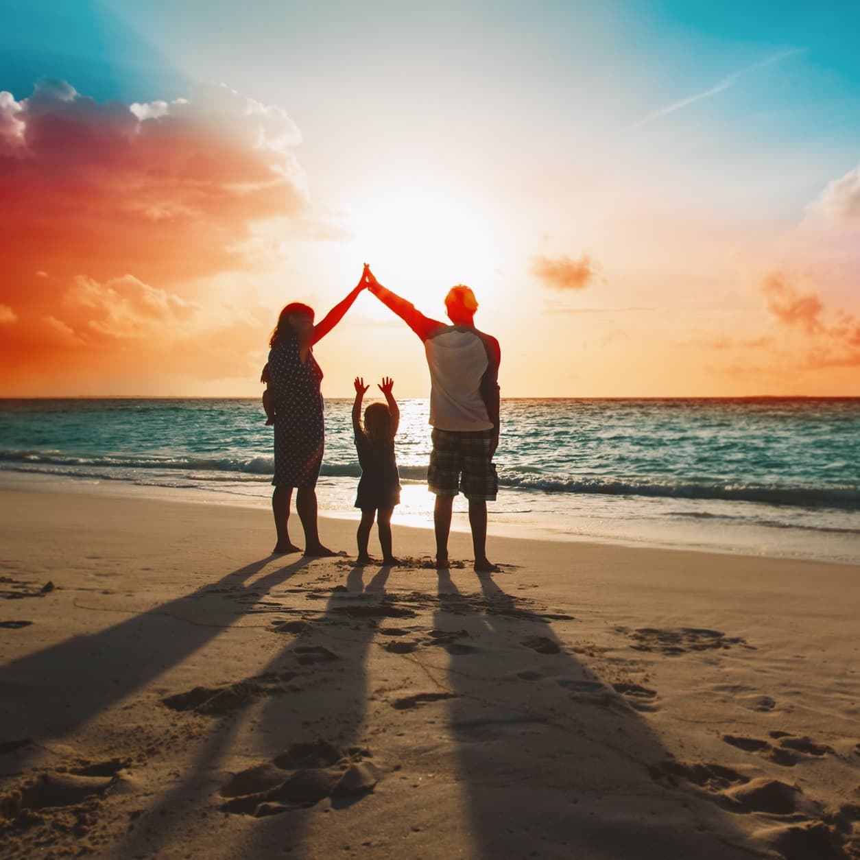 Family on a beach at sunset, the parents' hands raised together above their child