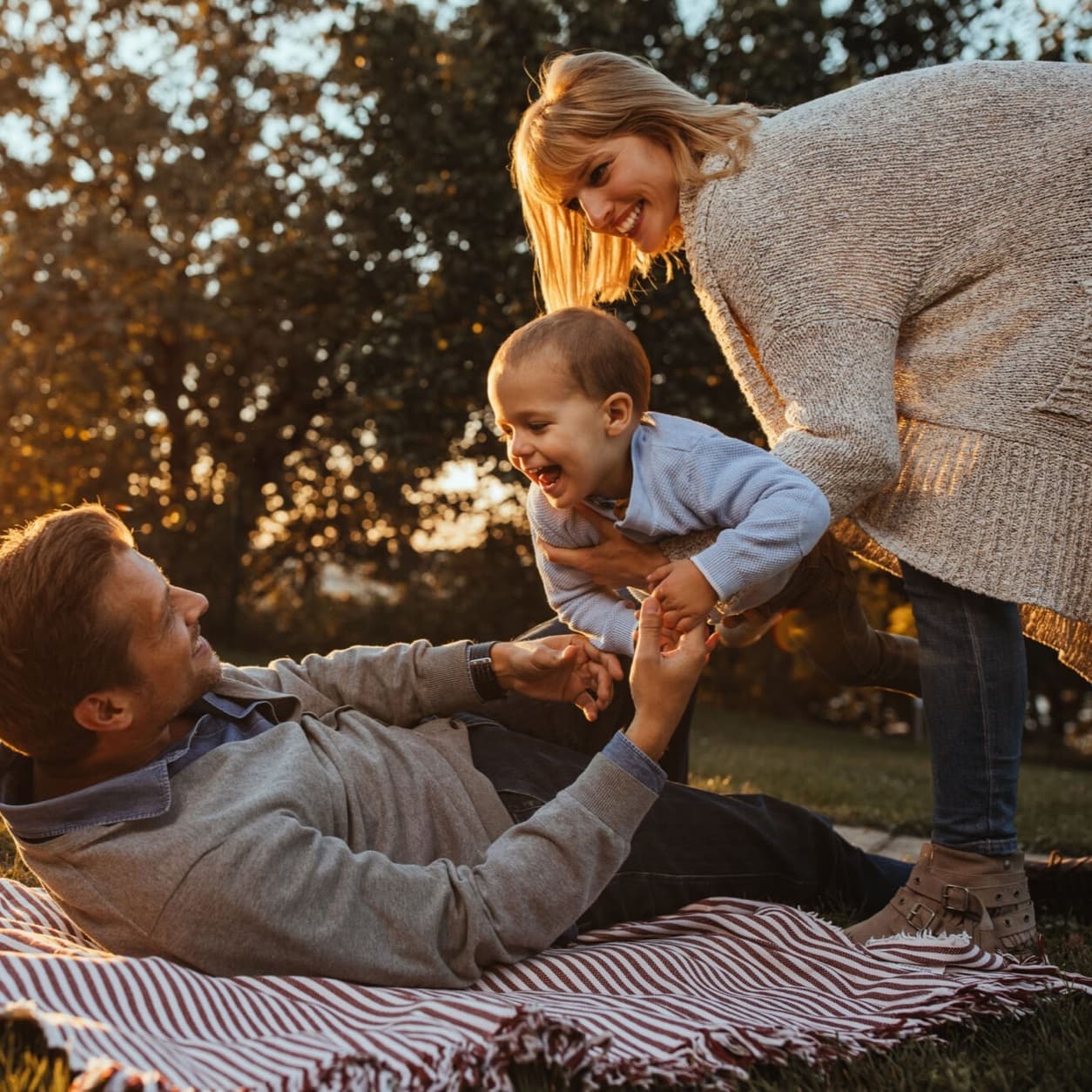 Father playing with his toddler on a picnic blanket while the mother holds them
