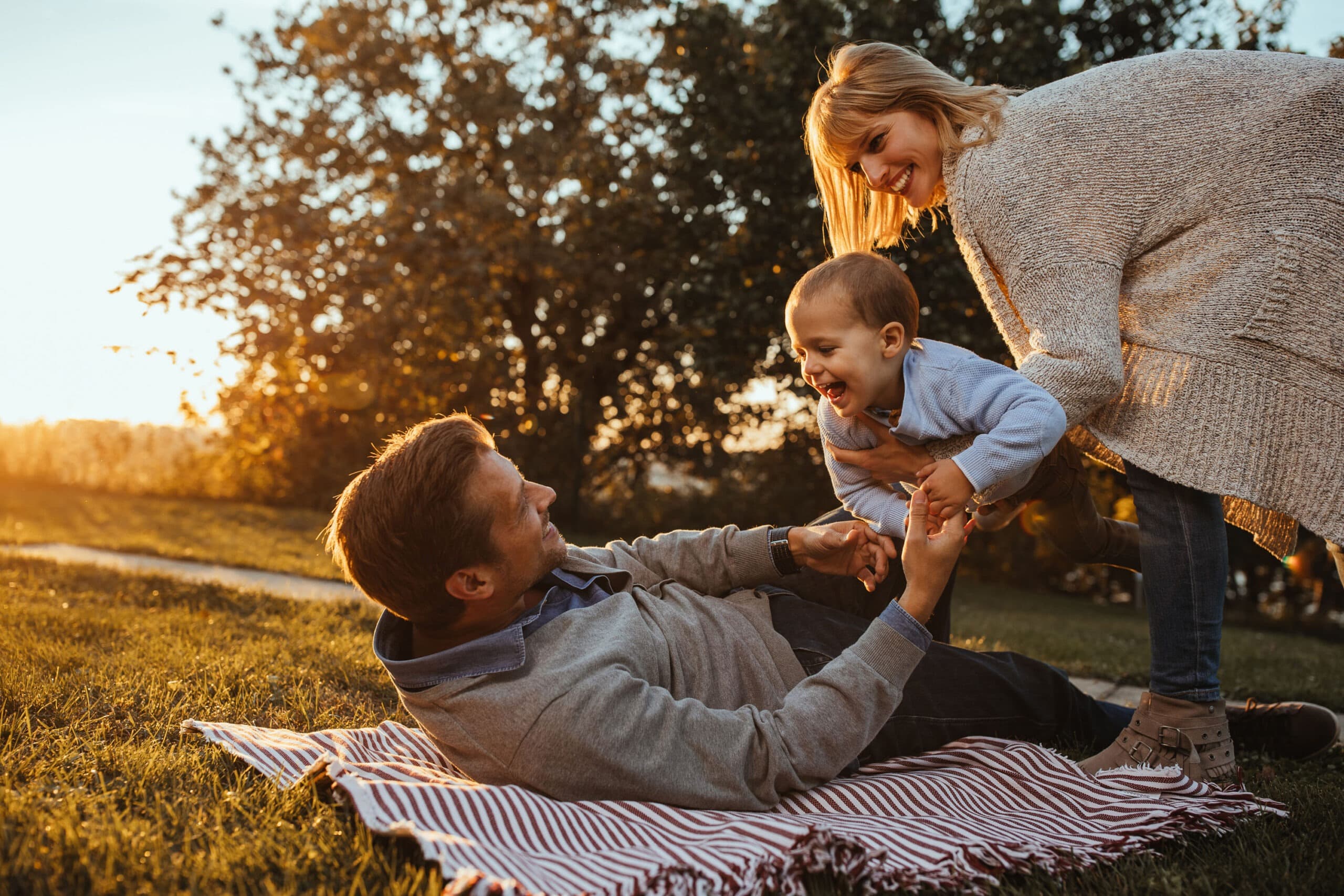 Father playing with his child outdoors while the mother looks on
