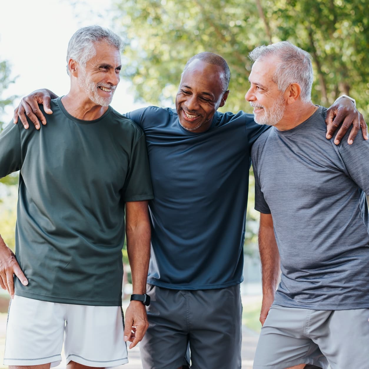 Three older men walking arm in arm along a park path