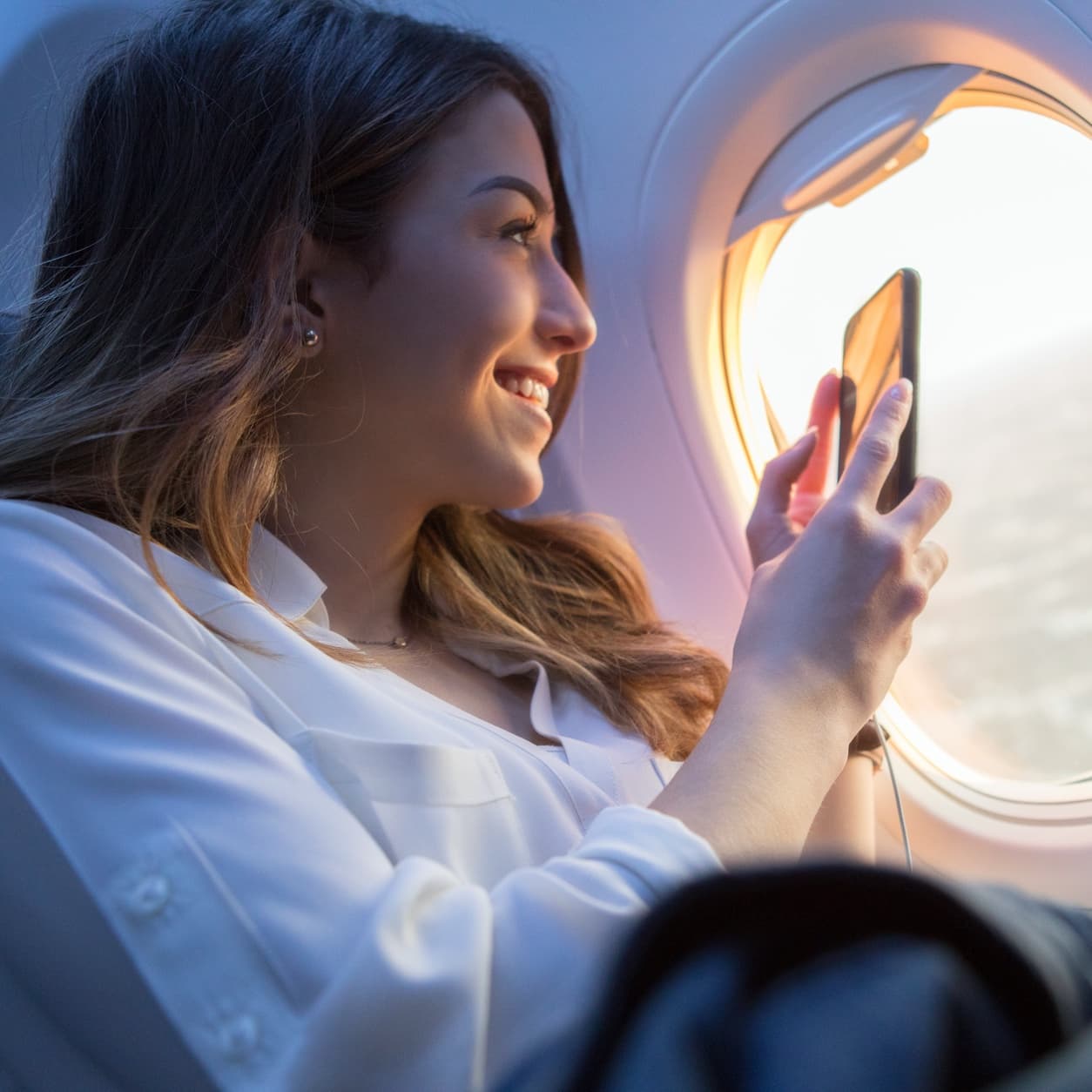 Woman photographing the sunset from an airplane window seat