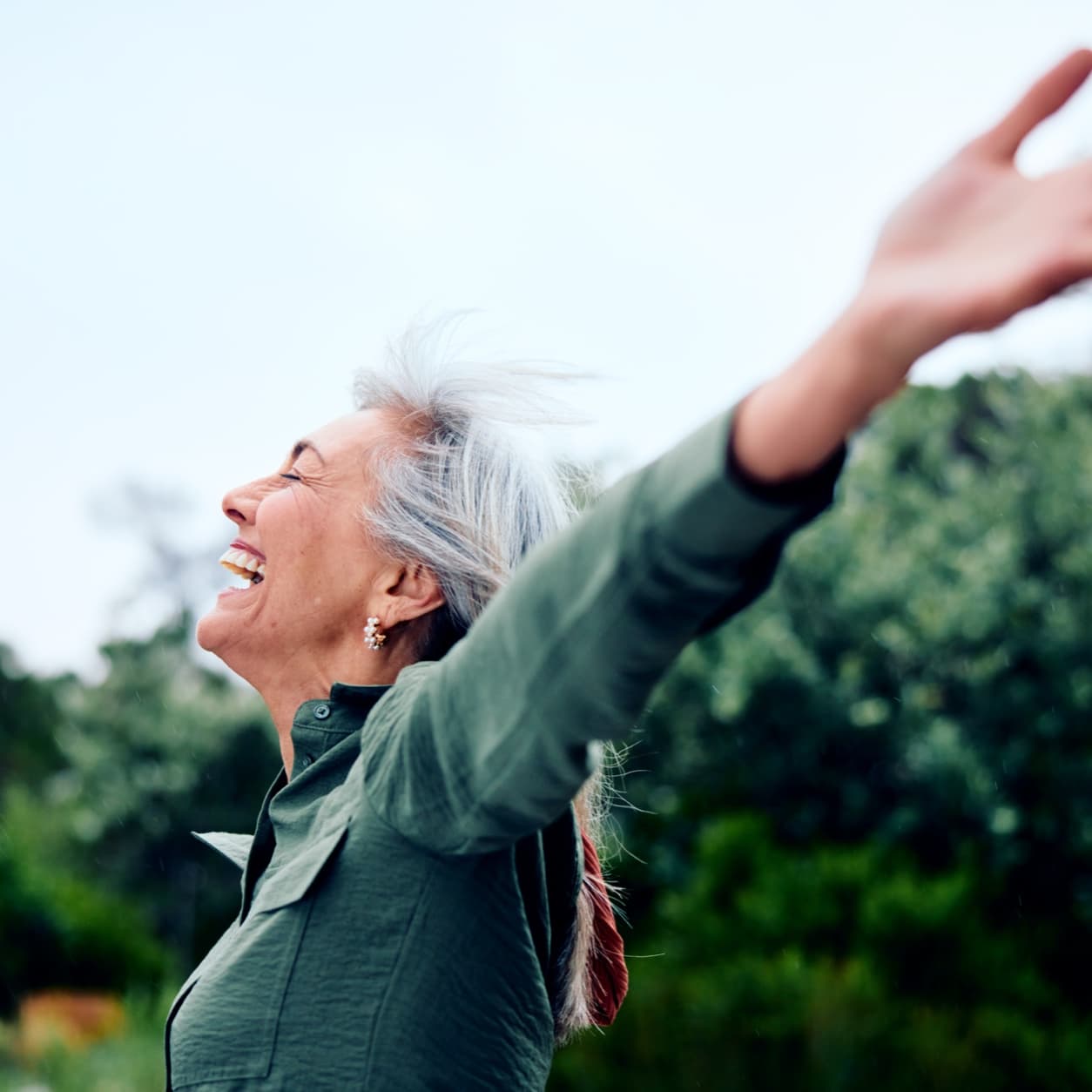 Older woman laughing with her arm outstretched outdoors